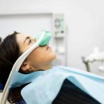 Dental professional administering nasal sedation mask to patient in dental chair