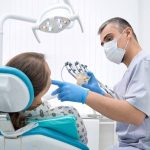 Dentist in mask and blue gloves shows a dental model to a smiling young woman in a dental chair